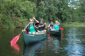 Quatre personnes dans des canoës sur une rivière paisible, entourée d’une végétation luxuriante.