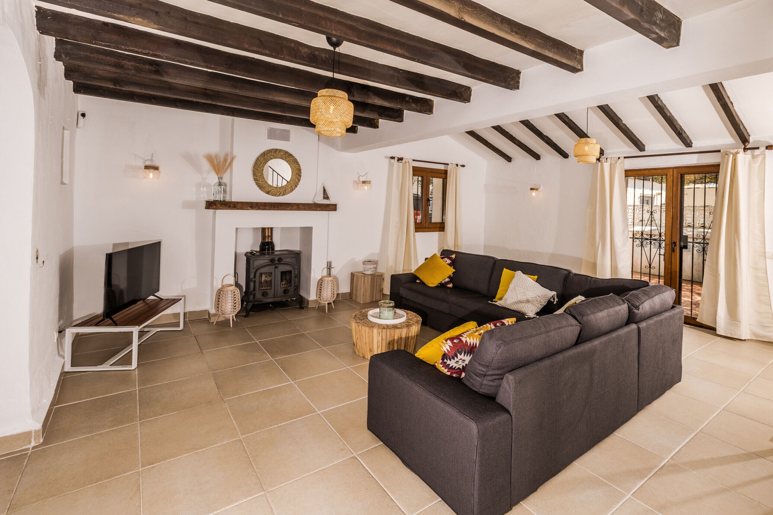Un salon avec un canapé foncé, un téléviseur, une cheminée et un balcon avec des rideaux.