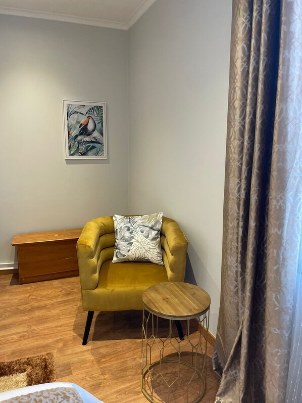 A room with a yellow armchair, a small round wooden table, a bench, and a painting on the wall.