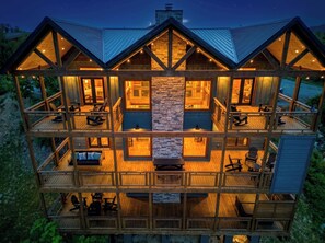 A multi-level wooden cabin with a stone fireplace, outdoor seating, and a balcony.