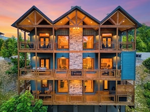 A multi-story log cabin with balconies, large windows, and a stone fireplace.
