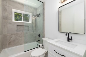 Une salle de bain moderne avec une douche à parois de verre, des toilettes blanches et un meuble-lavabo avec un miroir.