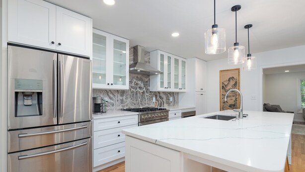 A modern kitchen with stainless steel appliances, white cabinetry, and a marble backsplash.