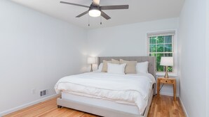 A bedroom with a bed, a ceiling fan, a window, and a nightstand.