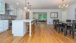 A modern kitchen with white cabinetry, a marble backsplash, and wooden flooring. There is a dining area with a dark wooden table and chairs.