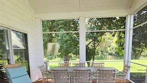 Une terrasse couverte avec un ventilateur de plafond, un plancher en bois et du mobilier d’extérieur comprenant un fauteuil à bascule et une table avec des chaises.