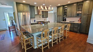 Une cuisine spacieuse avec un grand îlot central, des chaises en bois et des meubles de couleur vert foncé.