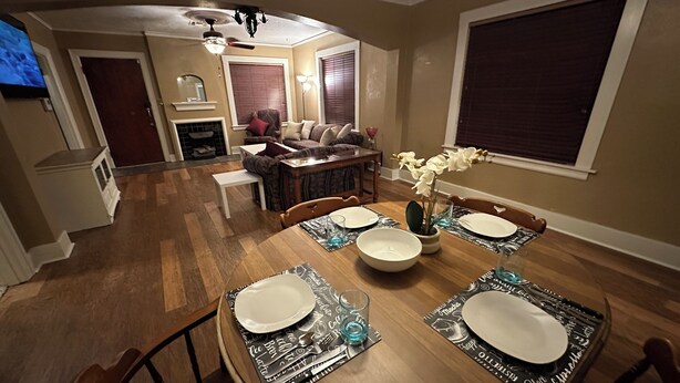 A dining area with a round table set for four, a fireplace, a sofa, and a television in the background. - Stay in Our Quaint Cottage Retreat for a Memorable Escape! (Duncan)