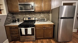 A kitchen with wooden cabinets, a stainless steel refrigerator, a microwave, a stove, and a toaster. - Stay in Our Quaint Cottage Retreat for a Memorable Escape! (Duncan)
