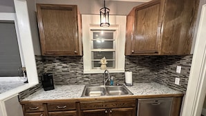 A compact kitchen with wooden cabinets, a stainless steel sink, and a dishwasher. - Stay in Our Quaint Cottage Retreat for a Memorable Escape! (Duncan)