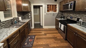 A kitchen with wooden cabinets, a stainless steel sink, a microwave, a stove, and a ceiling fan. - Stay in Our Quaint Cottage Retreat for a Memorable Escape! (Duncan)
