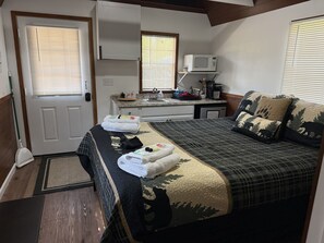 A compact room with a bed, a microwave, a small kitchenette, and a door.