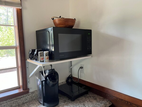 Una cocina con microondas sobre un estante blanco, cafetera y hervidor.