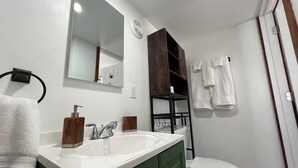 A bathroom with a white sink, green cabinet, and a white toilet. There is a mirror above the sink and a towel rack with towels.