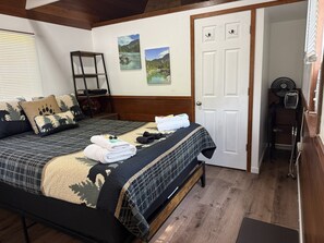 A bedroom with a bed, a bench, a fan, and a door.