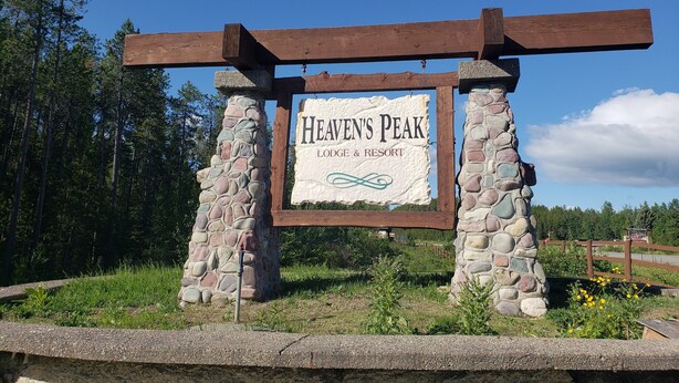 A stone and wooden sign for Heaven's Peak Lodge & Resort with a clear sky and forest in the background.