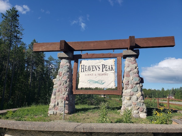 Letrero de piedra y madera para Heaven's Peak Lodge & Resort, con cielo despejado y bosque al fondo.