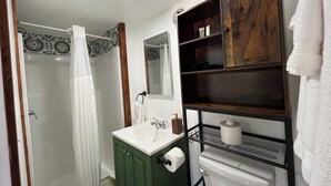 A bathroom with a shower, toilet, sink, and a wooden shelf with toiletries.