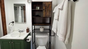 A bathroom with a green cabinet, white sink, and a toilet. There is a towel rack with towels and a mirror above the sink.