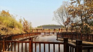 A wooden bridge over a calm body of water, surrounded by trees and a distant building. - Jinjiang Inn (Xinyi Zhongwu Road) (Xinyi)