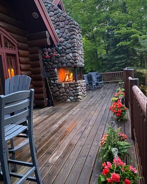 Une cabane en rondins avec une cheminée en pierre, une terrasse en bois et un espace salon extérieur.
