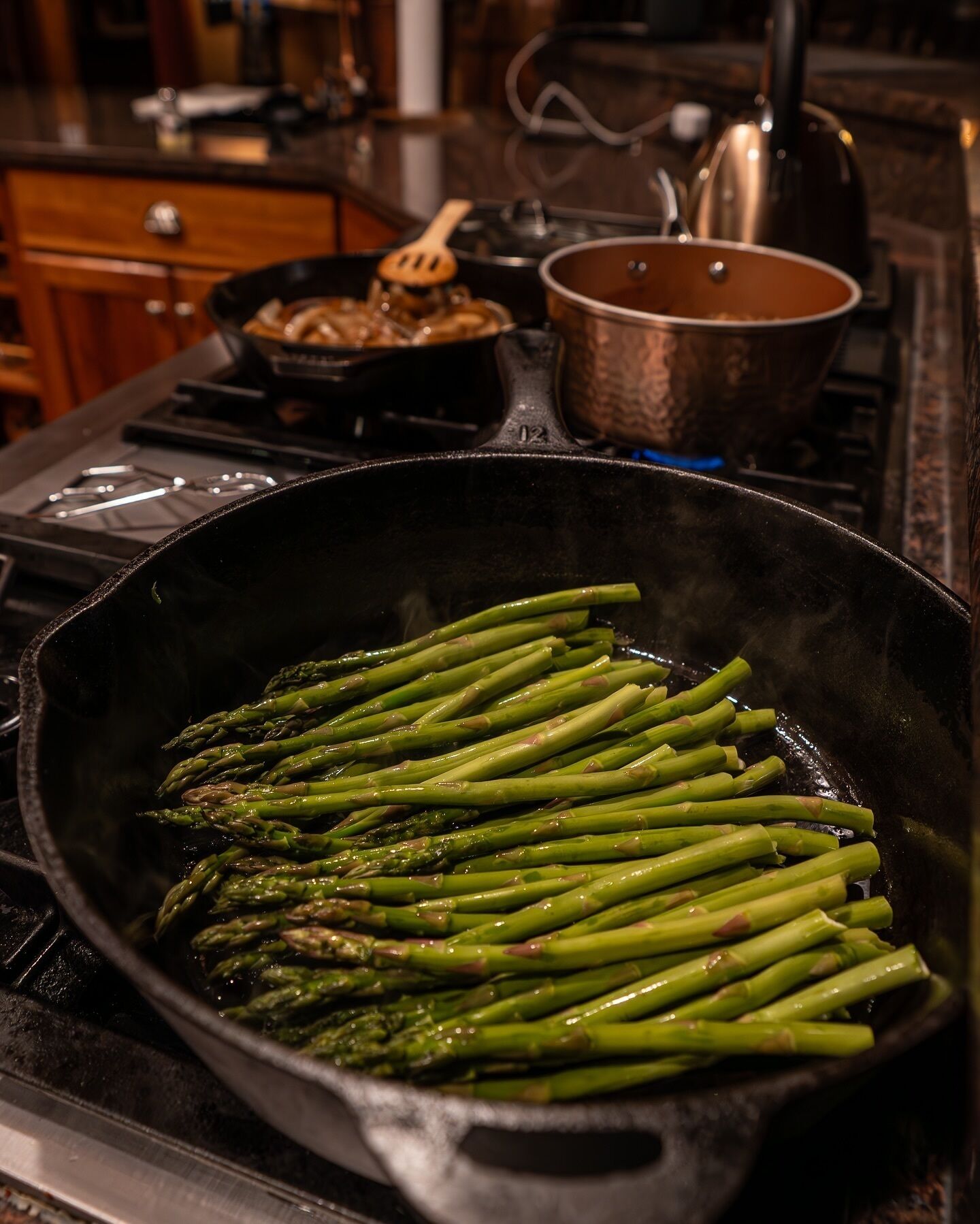 Een keuken met een gietijzeren pan op het fornuis met asperges.