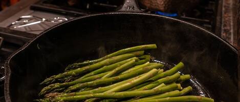 A kitchen with a cast iron skillet on a stove containing asparagus.