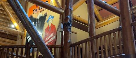 A rustic interior with exposed wooden beams, a wooden staircase, and a dining area with tables and chairs.