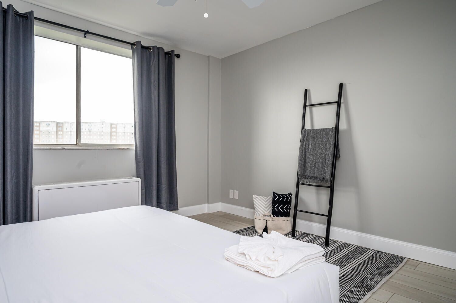 Habitació d'hotel amb un llit gran, una finestra amb cortines, un radiador, una escala negra i una catifa estampada.
