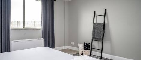 Habitación de hotel con una cama grande, una ventana con cortinas, un radiador, una escalera negra y un tapete estampado.