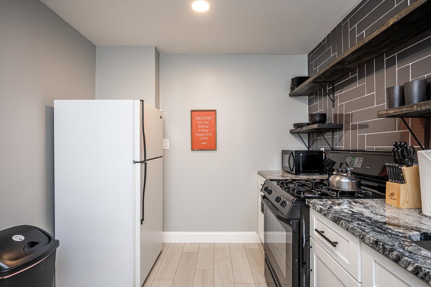 Une cuisine compacte avec un réfrigérateur blanc, une cuisinière, un four à micro-ondes et une planche à découper en bois avec des couteaux.