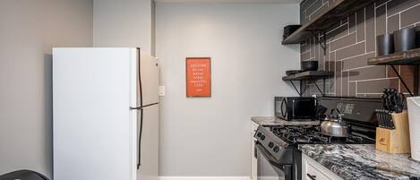 Una cocina compacta con un refrigerador blanco, estufa, microondas y tabla de cortar de madera con cuchillos.