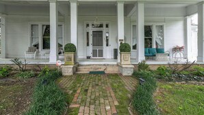 A white porch with columns, a front door, and a small step leading to a front porch area with a bench and a chair. - 1883 Colonial Revival Historical Renovation  (Mount Pleasant)
