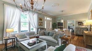 A living room with a sofa, coffee table, and chandelier. There is a dining area with a table and chairs. - 1883 Colonial Revival Historical Renovation  (Mount Pleasant)