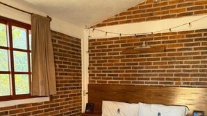 A bedroom with a brick wall, wooden headboard, and a bed with a grey blanket.