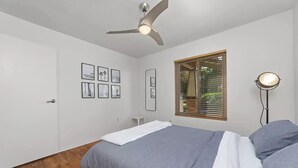 Camera da letto con un letto, una ventola a soffitto, una finestra con persiane e quadri appesi al muro.