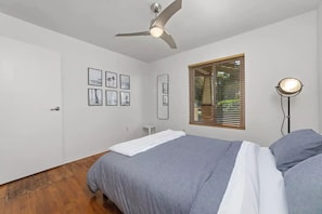 Un dormitorio con una cama, un ventilador de techo, una ventana con persianas y cuadros en la pared.