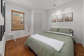 A bedroom with a bed, a window with blinds, a door, and three framed pictures on the wall.