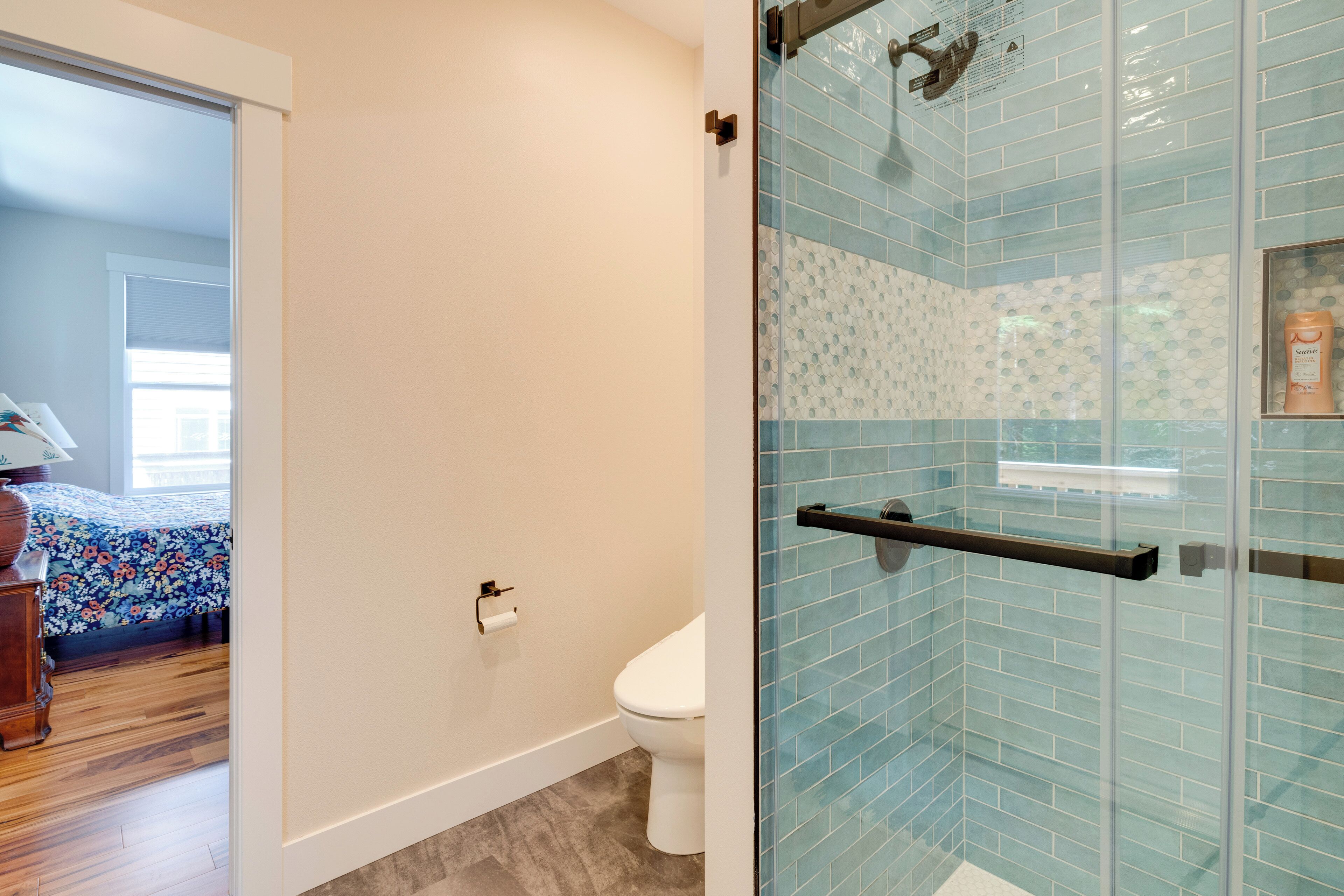 A bathroom with a glass shower enclosure, a toilet, and a wooden floor.