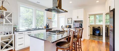 A modern kitchen with a central island, bar stools, a built-in oven, and a large window.