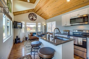 A spacious kitchen with a large island, stainless steel appliances, and a wooden ceiling. - 2 Mi to Rainbow Lake: Lovely Lakeside Tiny Home (Lakeside)