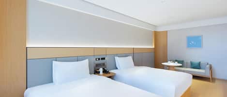Een hotelkamer met twee bedden, een nachtkastje met telefoon en lamp, een klein tafeltje met lamp, en een bank.
