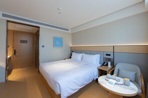 A hotel room with a bed, bedside table, chair, and a small table with a phone, kettle, and cups. - Ji Hotel Hangzhou Jiaogong Road (Hangzhou)