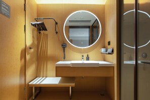A compact, modern bathroom with a wooden vanity, a round mirror, a towel rack, and a small shelf with toiletries. - Ji Hotel Hangzhou Jiaogong Road (Hangzhou)