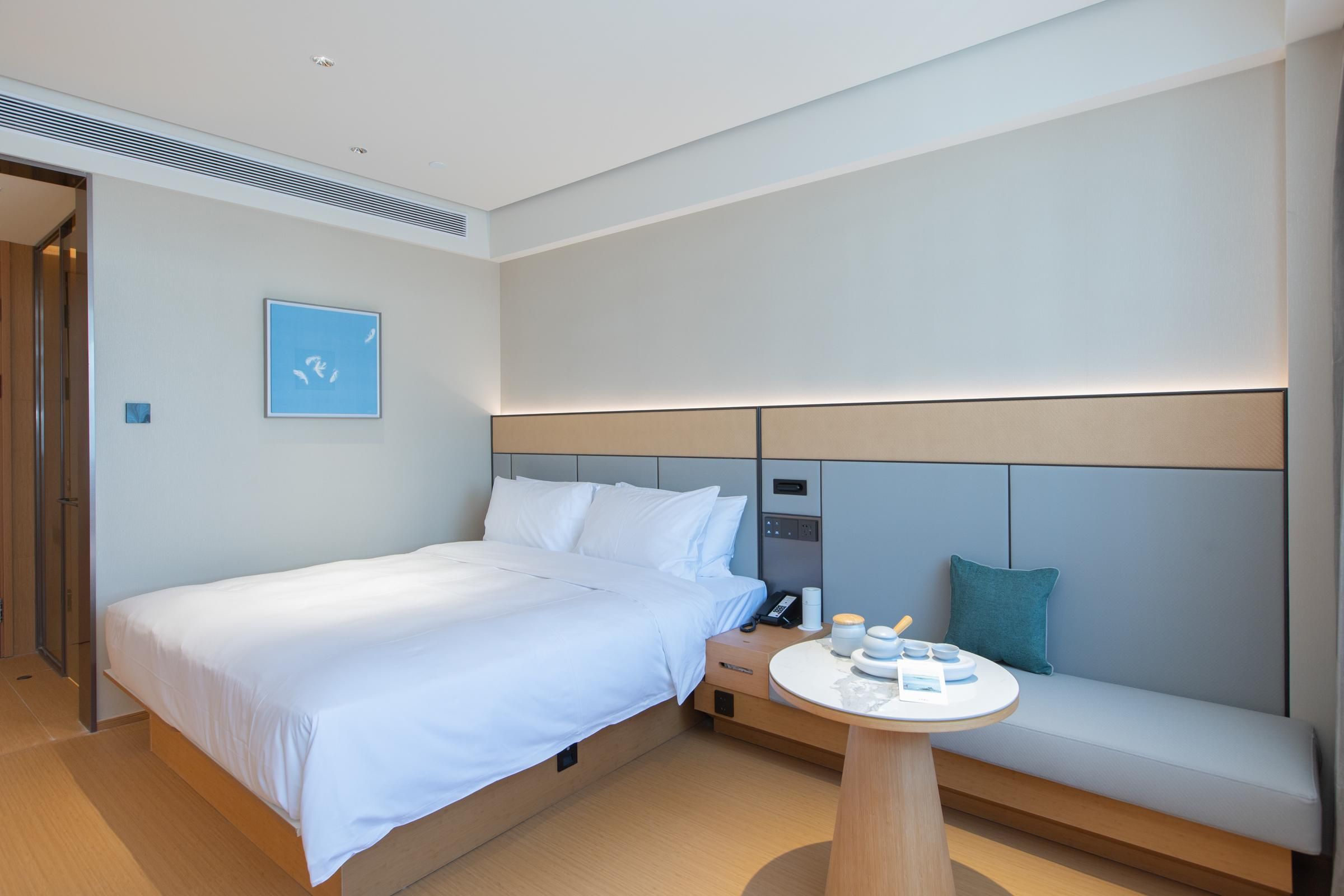 Una habitación de hotel moderna con una cama grande, una mesita de noche con detalles, un banco incorporado y una pequeña mesa redonda.