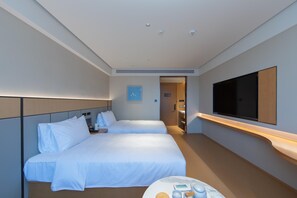 A hotel room with two beds, a TV mounted on the wall, and a small table with toiletries.