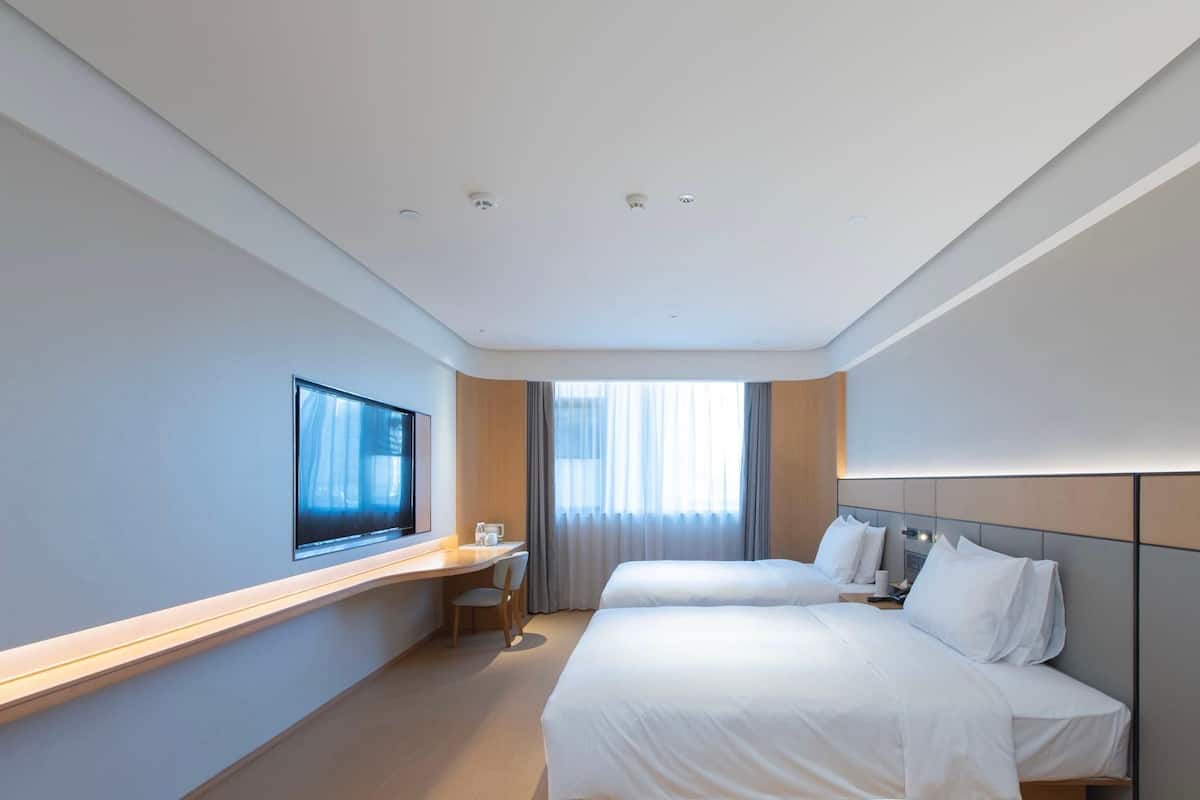 A hotel room with two beds, a TV, a desk, and a window with curtains.