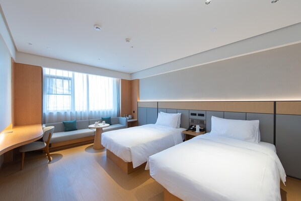 A modern hotel room with two beds, a desk, a sofa, and a small table.