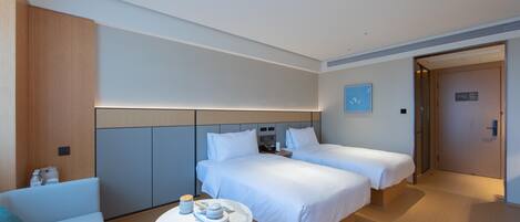 A modern hotel room with two beds, a small table with a cup and saucer, and a sofa.