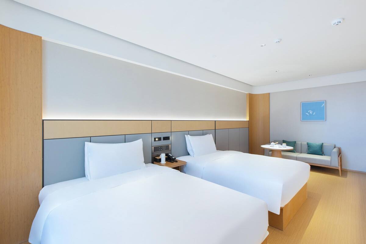 A modern hotel room with two beds, a small table, and a sofa.